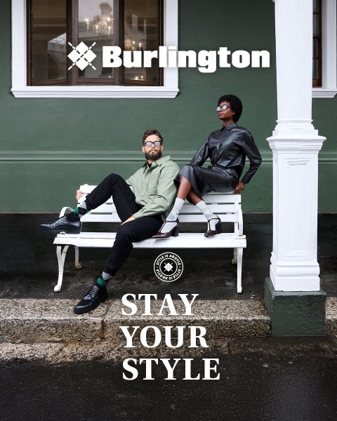 Un uomo e una donna in abiti eleganti posano con sicurezza su una panchina bianca davanti a un muro verde con i testi "Burlington" e "Stay Your Style" sopra e sotto di loro.