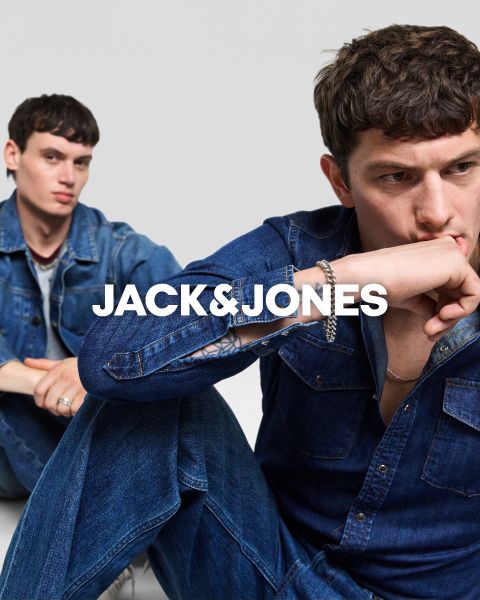 Due uomini in abiti di jeans siedono davanti a uno sfondo semplice. L'uomo davanti si tiene una mano sulla bocca, mentre l'altro è seduto dietro di lui. Al centro c'è il testo "JACK & JONES".