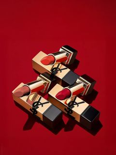 Tre rossetti dorati e neri con diverse tonalità di rosso disposti diagonalmente su uno sfondo rosso tinta unita. La confezione è decorata con un logo nero sull'involucro dorato.