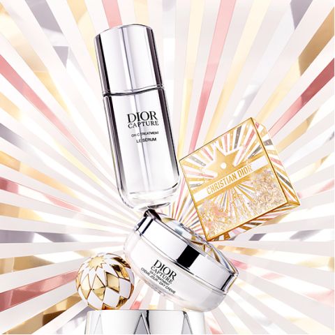 Due prodotti per la cura della pelle Dior e un cofanetto dorato per il trucco Christian Dior sono presentati su uno sfondo radioso con motivi a raggiera dorati, rosa e bianchi, creando un effetto lussuoso e luminoso.