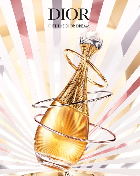 Un flacone dorato di profumo Dior con anelli a spirale su uno sfondo radioso con alba. Il testo sopra recita: "DIOR" e "REGALA IL SOGNO DIOR".