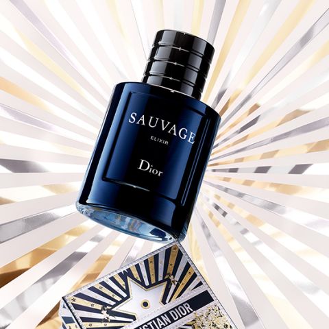 Un flacone blu scuro del profumo Dior Sauvage Elixir è esposto davanti a uno sfondo luminoso con cielo stellato, con una mappa decorativa di Christian Dior parzialmente visibile in basso.
