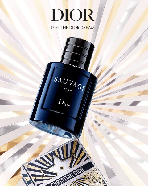 Un flacone del profumo Dior Sauvage Elixir è posizionato sopra una scatola decorativa Dior, da cui emergono raggi dorati, argentati e bianchi sullo sfondo. Il testo recita: "Dior. Regala il sogno Dior."