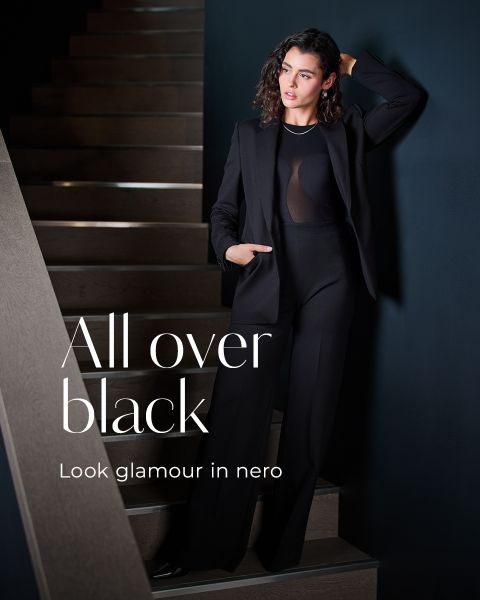 Una donna in un elegante outfit nero è appoggiata a un muro scuro accanto a una scala. Il testo sull'immagine recita: "All over black. Look glamour in Nero".