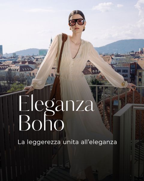 Eine Frau in einem fließenden cremefarbenen Kleid und mit Sonnenbrille steht auf einem Balkon mit Blick auf eine Stadt. Auf dem Bild ist der Text "Eleganza Boho" in italienischer Sprache zu lesen.