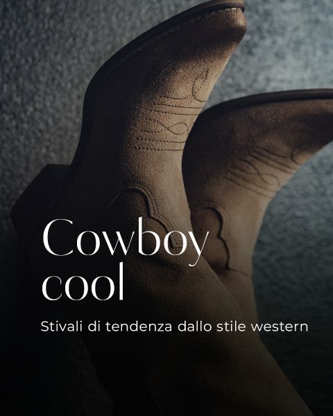 Primo piano di due stivali da cowboy marroni in pelle scamosciata con cuciture decorative su una superficie grigia strutturata. Il testo sovrapposto in italiano recita "Cowboy cool. Stivali di tendenza dallo stile western.".