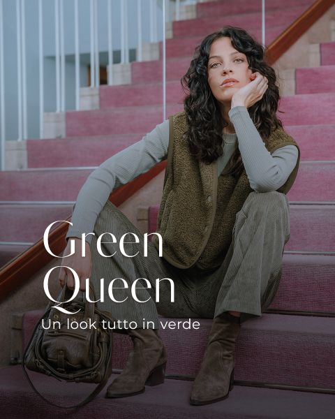 Una donna con capelli scuri ondulati è seduta su una scalinata rosa, indossa abiti colorati di verde e stivali marroni e ha una borsa marrone accanto a sé. Il testo dice: "Regina verde. Un look tutto in verde."