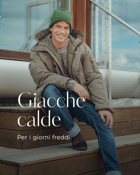 Un uomo sorridente con un berretto di lana verde, giacca invernale beige, maglione, jeans e stivali è seduto su una scala di legno. Giacche calde. Per i giorni freddi.