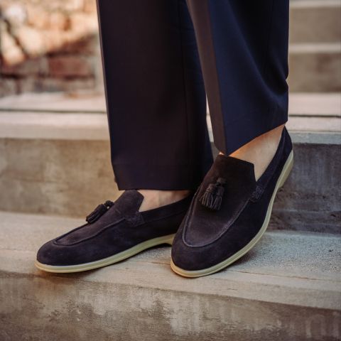 Una persona che indossa scarpe scamosciate nere con nappe e pantaloni scuri è in piedi su una scala di cemento all'aperto.