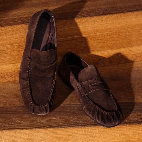 Un paio di scarpe scamosciate marroni esposte su gradini di legno, la cui trama è messa in risalto da luci e ombre.