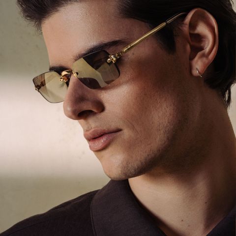 Uomo con occhiali da sole con montatura dorata e camicia scura.