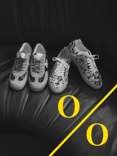 Una foto in bianco e nero di due paia di scarpe da ginnastica fantasia su un sedile in pelle nera. Una linea diagonale gialla con due lettere "O" gialle adorna l'angolo inferiore destro dell'immagine.