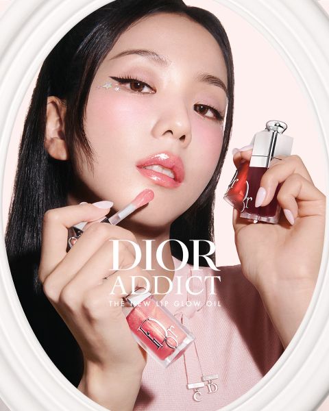 Una donna indossa un lucidalabbra rosa mentre tiene in mano un flacone di Dior Addict Lip Glow Oil, con un trucco rosa tenue e un adesivo a forma di stella vicino all'occhio.