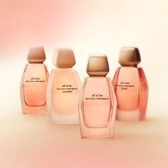 Quattro flaconi del profumo "All of Me" di Narciso Rodriguez in delicate tonalità di rosa e beige, disposti davanti a uno sfondo chiaro, leggermente sfocato.