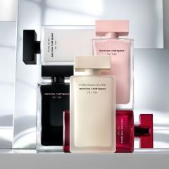 Cinque flaconi di profumo di Narciso Rodriguez in nero, bianco, rosa e rosso sono disposti in verticale e impilati davanti a uno sfondo moderno e riflettente.