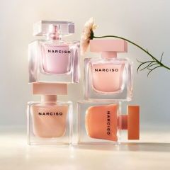 Quattro flaconi di profumo del marchio Narciso in tonalità pastello sono impilati uno sull'altro, e un singolo fiore bianco si inclina da destra.