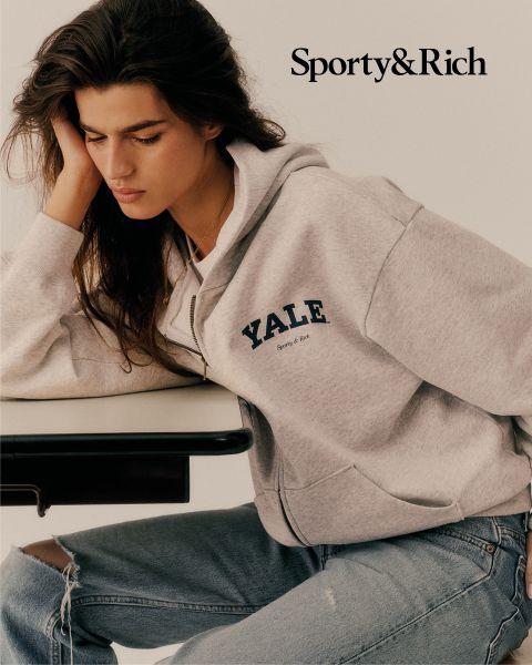 Una persona con una felpa grigia YALE e jeans strappati è seduta a un tavolo e guarda pensierosa verso il basso. Nell'angolo in alto a destra c'è scritto "Sporty & Rich".
