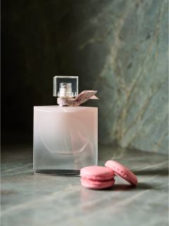 Un flacone di profumo rosa con un fiocco si trova accanto a due macarons rosa su una superficie di marmo.