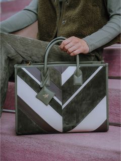 Persona con una grande borsa a tracolla a motivi geometrici nei toni del verde, bianco e grigio, seduta su gradini rosa.