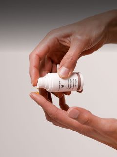 Una persona versa una piccola quantità di crema o lozione da una bottiglia bianca sulla punta del dito.