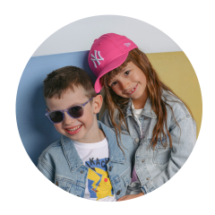 Due bambini sorridenti con giacche di jeans; il ragazzo indossa occhiali da sole, la ragazza un cappellino da baseball rosa e appoggia la testa sulla sua.