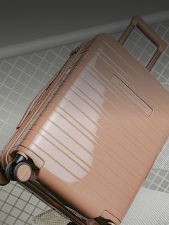 Una valigia rigida lucida, marrone chiaro, con ruote e maniglia estraibile è appoggiata su una superficie piastrellata.