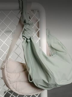 Due borse a tracolla, una beige chiaro e una verde pallido, sono appese a una griglia metallica bianca su uno sfondo neutro.