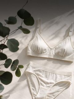 Un set color crema di reggiseno e slip è adagiato su una superficie chiara su cui si proiettano ombre di foglie.