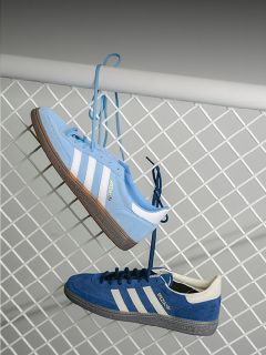 Due scarpe da ginnastica Adidas blu con strisce bianche sono appese ai lacci a una recinzione di metallo bianca, una azzurra e una blu scuro.