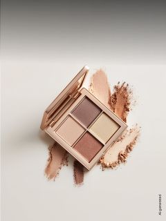 Una palette di ombretti aperta con quattro tonalità neutre, circondata da campioni delle polveri su una superficie chiara.