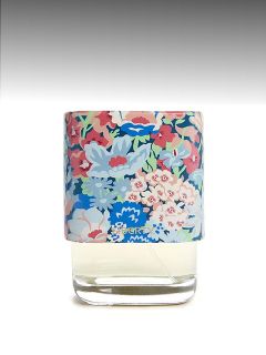 Un flacone di profumo in vetro con un tappo colorato a motivi floreali su uno sfondo grigio sfumato.