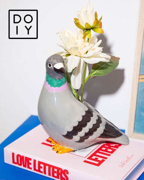 Vaso a forma di colomba in ceramica con fiori bianchi su un libro "Love Letters", con un logo DOIY nell'angolo in alto a sinistra.