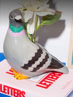 Una figura di colomba in ceramica con un fiore bianco è appoggiata su un libro intitolato "LETTERS" con una copertina bianca e rossa.