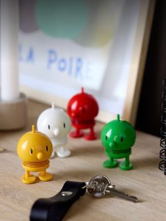 Quattro figure giocattolo colorate e rotonde sono su una scrivania accanto a chiavi e un quaderno, con un'opera d'arte incorniciata sfocata sullo sfondo.