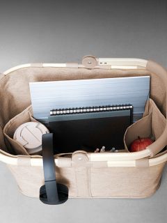 Un cesto beige contiene un laptop, un quaderno, penne, una tazza da viaggio bianca e una mela rossa, visto dall'alto.