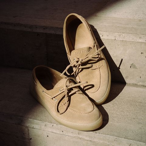 Scarpe da barca beige in pelle scamosciata con lacci appoggiate su gradini di cemento nella luce soffusa del sole.