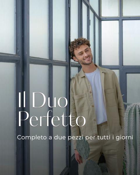 Un uomo in un completo a due pezzi beige chiaro sorride davanti a grandi finestre. Testo: "Il Duo Perfetto. Completo a due pezzi per tutti i giorni."