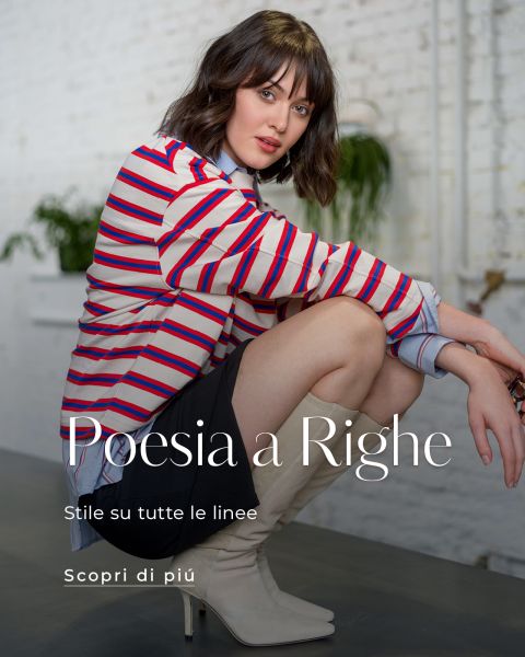 Una donna con i capelli castani corti indossa una camicia a righe, una gonna nera e stivali beige ed è seduta in una casa. Testo: "Poesia a Righe. Stile su tutte le linee. Scopri di più.