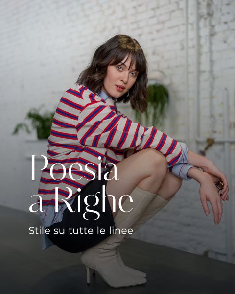 Frau in gestreiftem Hemd und weißen Stiefeln, die in einem Haus kauert, mit Text in italienischer Sprache "Poesia a Righe. Stile su tutte le linee" über dem Bild.