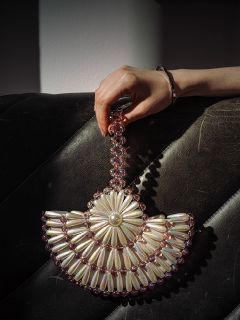 Una mano tiene una borsetta di perline con motivi di perle e fiori rosa, appoggiata su una superficie in pelle nera strutturata.
