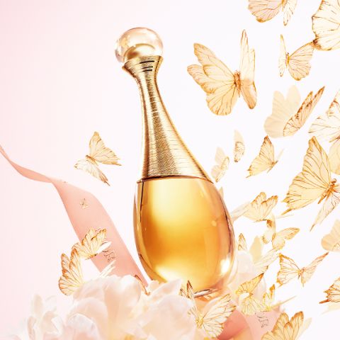 Flacone di profumo dorato, circondato da un nastro rosa, fiori bianchi e farfalle dorate svolazzanti su uno sfondo pastello.