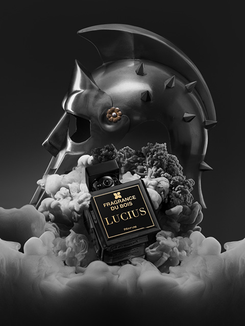 In mezzo al fumo si erge una boccetta di profumo nera con la scritta „Fragrance Du Bois Lucius“, sullo sfondo è visibile un elmo da gladiatore metallico.