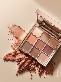 Una palette di ombretti con nove tonalità in colori caldi e neutri, con un po' di polvere sparsa su una superficie beige.
