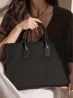 Una donna con un maglione marrone tiene una grande borsa nera con due manici e ha una coperta bianca sulle ginocchia.