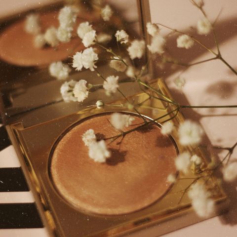 Un evidenziatore dorato e compatto con piccoli fiori bianchi sulla punta, che si riflettono in uno specchio e creano un'estetica delicata ed elegante.