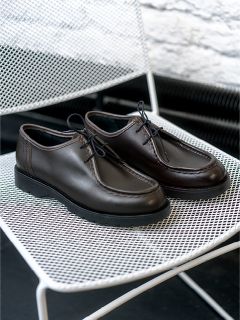 Un paio di scarpe stringate in pelle marrone scuro sono appoggiate su una sedia di metallo bianco con griglia.