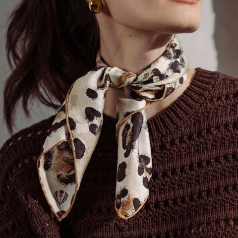 Una donna indossa un maglione di lana marrone e una sciarpa color crema con stampa leopardata legata al collo.