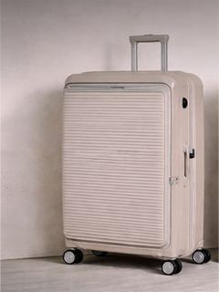 Valigia rigida beige con scanalature orizzontali, in posizione verticale su quattro ruote, con maniglia telescopica estesa.