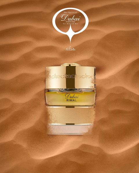 Un flacone di profumo dorato con la scritta „Dubai Rimal“ è parzialmente immerso nella sabbia liscia del deserto, sopra di esso c'è la scritta „The Spirit of Dubai“.