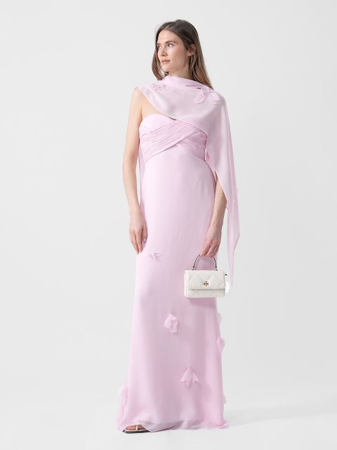 Una donna in un abito rosa chiaro senza spalline con dettagli floreali tiene una piccola borsa bianca e indossa uno scialle trasparente abbinato su una spalla.